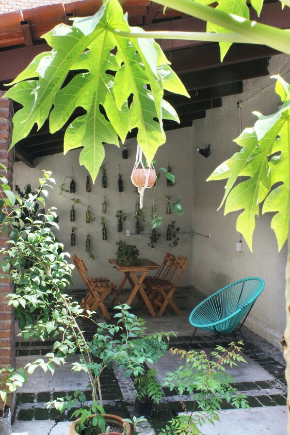 Un patio con una mesa y sillas, rodeado de plantas en macetas y jardineras colgantes.