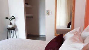A bedroom with a large bed, a bedside table with a potted plant, and a mirror on the wall.