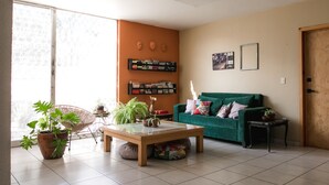 A living room with a green sofa, a wooden coffee table, a wicker chair, and a bookshelf with books and decorative items.