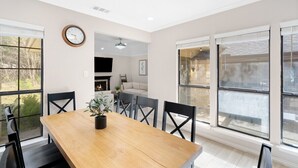 A dining area with a wooden table, black chairs, a potted plant, and large windows.