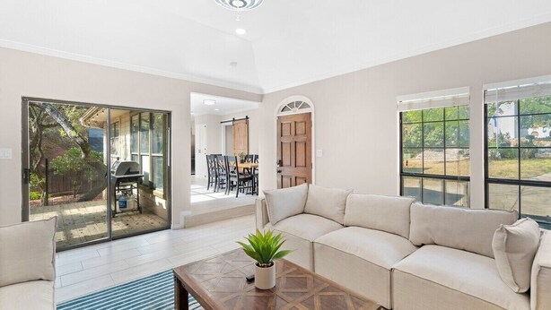 A spacious living room with a beige sofa, a coffee table with a plant, and large windows offering a view of the outdoors.