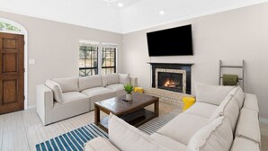 A living room with a beige sofa, a coffee table, a fireplace, and a TV mounted on the wall.