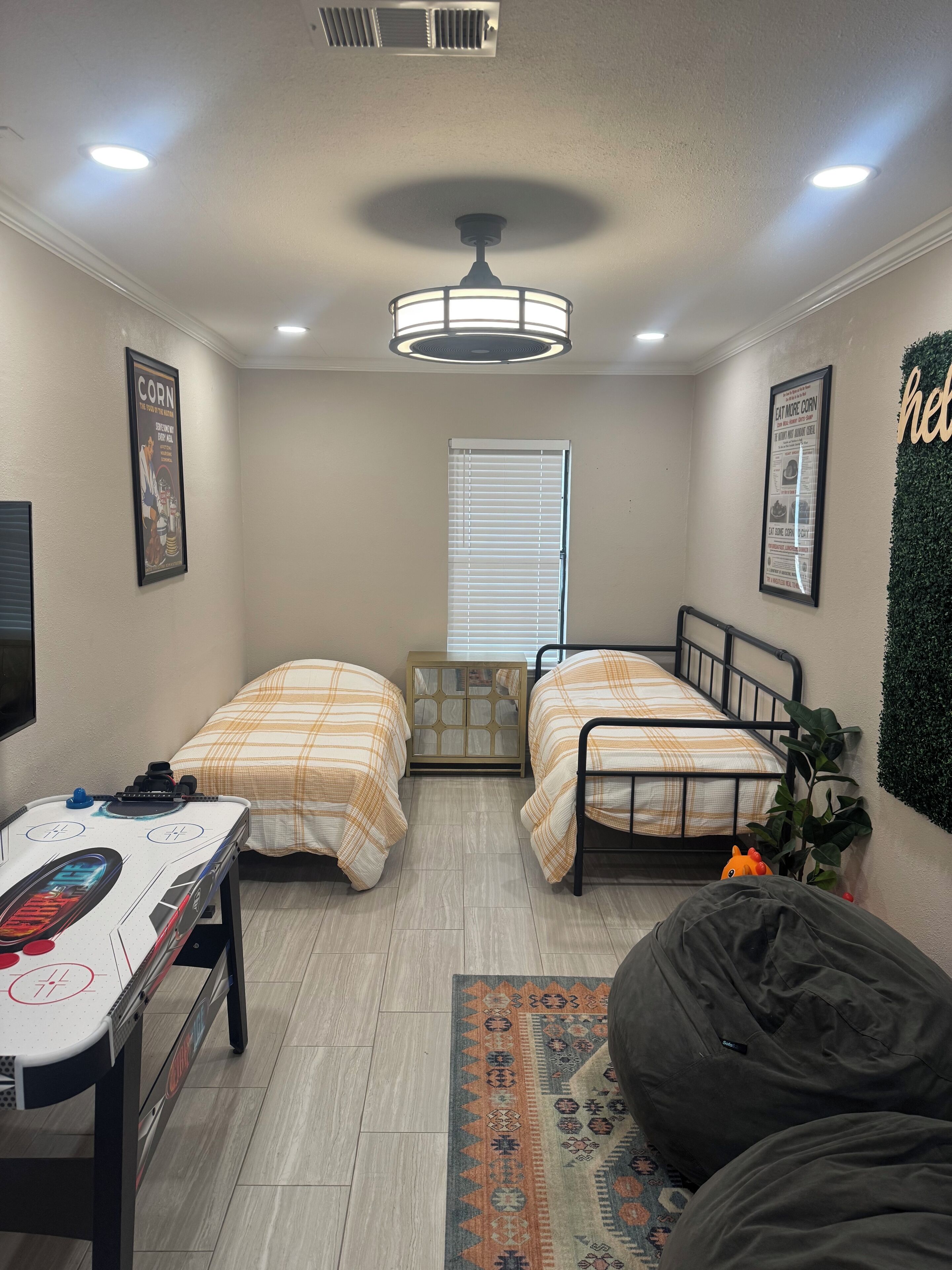 A small, well-lit room with two beds, a desk, a bean bag, and a radiator.