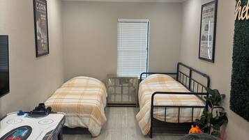A small, well-lit room with two beds, a desk, a bean bag, and a radiator.