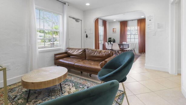 A living room with a brown leather sofa, a round wooden coffee table, and a teal armchair. There is a dining area in the background with a table and chairs. - Spacious Designed House -Palm Wave Stays (West Palm Beach)