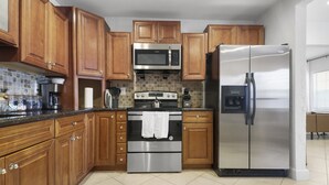 A kitchen with wooden cabinets, a stainless steel refrigerator, a microwave, and an oven. - Spacious Designed House -Palm Wave Stays (West Palm Beach)