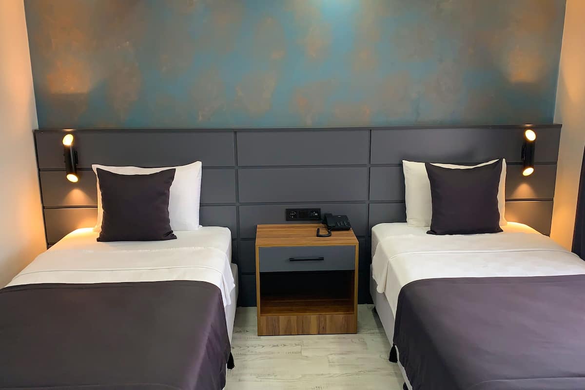 Quarto de hotel com duas camas, cada uma com almofada e mesa de cabeceira com telefone.