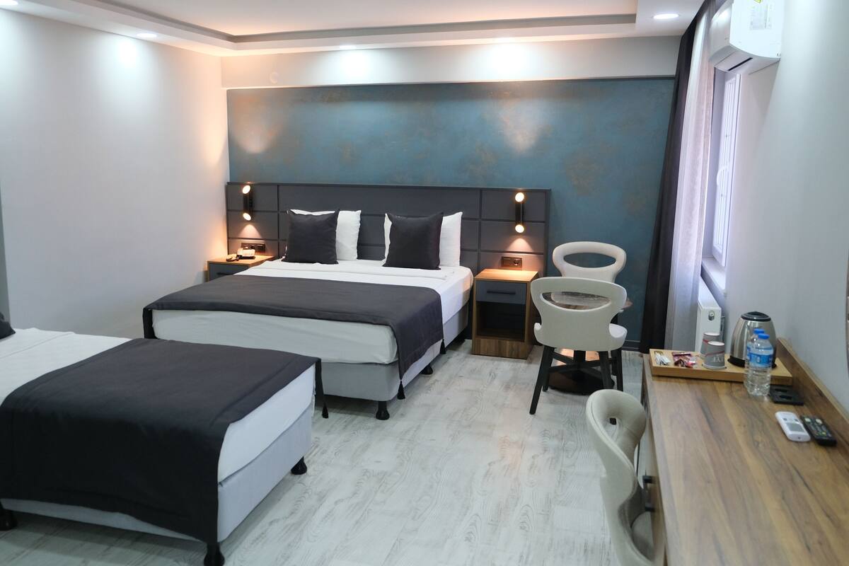 Quarto de hotel com duas camas, uma escrivaninha com cadeira, uma cafeteira e uma garrafa de água.