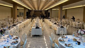 Un salón de banquetes con varias mesas redondas dispuestas para cenar, un escenario al frente y un techo alto con iluminación empotrada.