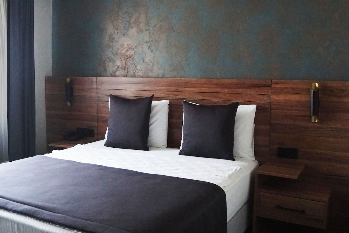 Cama bem arrumada com cabeceira de madeira, duas mesas de cabeceira e um criado-mudo.