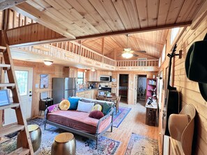 A cabin interior with a bed, kitchenette, and a dining area. - Texas Sun Cabin: Eight Acres with Trails and Amazing Sunset Views (Graham)