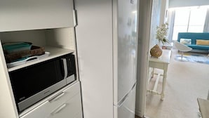 Une cuisine compacte dotée d’un micro-ondes et d’un réfrigérateur intégrés, d’un plancher en bois et donnant sur un espace de vie comprenant un canapé et une table.