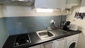 Une cuisine compacte équipée d’une cuisinière, d’un évier et d’un lave-linge.