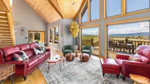 A spacious room with a wooden ceiling, large windows, a red leather sofa, a green armchair, and a view of the outdoors. - MAJESTIC VIEWS | Family Lodge | Large Deck (Star Valley Ranch)