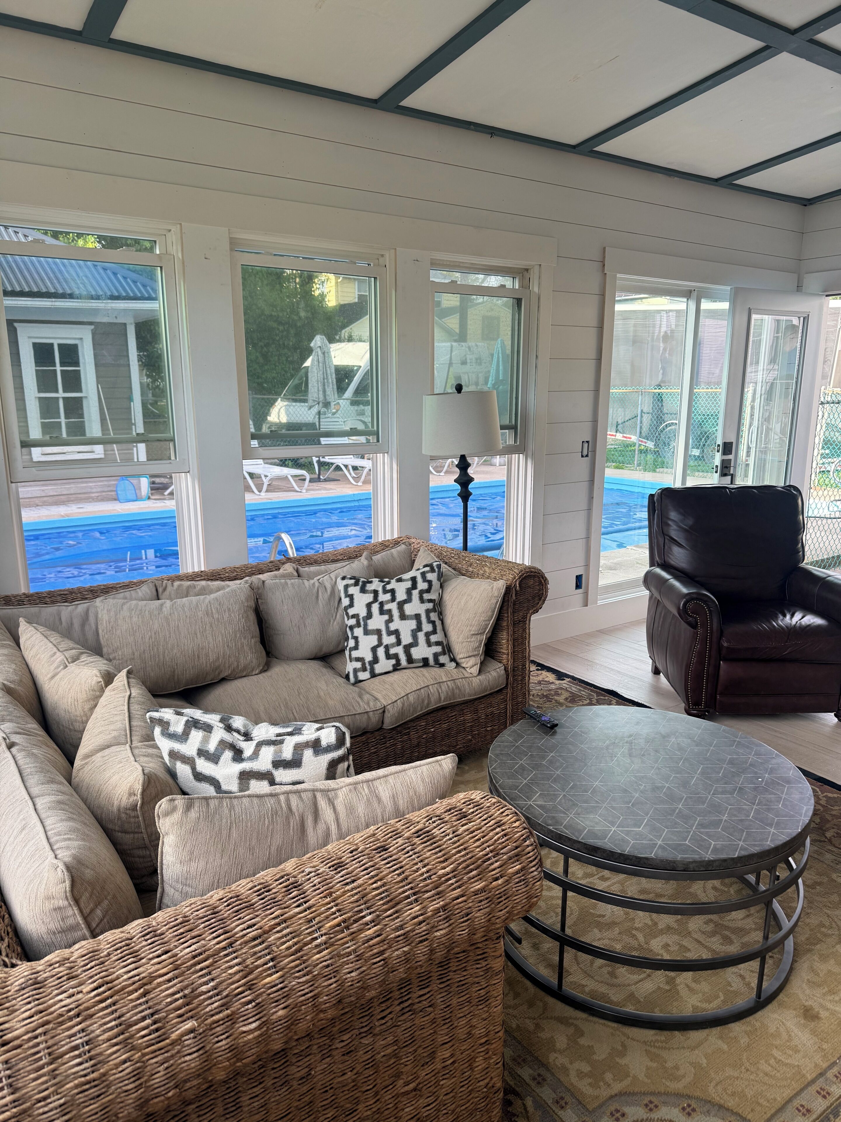 A covered outdoor seating area with a wicker sofa, a leather chair, and a round table.