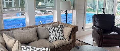 A covered outdoor seating area with a wicker sofa, a leather chair, and a round table.