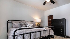 Une chambre à coucher avec un lit en métal, un ventilateur de plafond, une lampe de chevet et une armoire en bois.