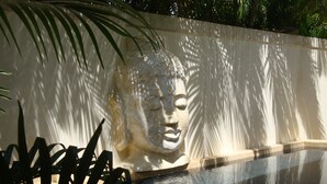 Un espace piscine paisible, agrémenté d’une grande sculpture ornée en arrière-plan, le tout entouré d’une végétation luxuriante.