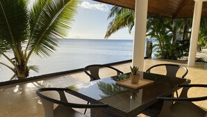 Un espace de restauration extérieur abrité, avec vue sur l’océan, comprenant une table à plateau en verre et quatre chaises.