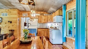 A cozy cabin-style kitchen with wooden cabinets, a dining table with chairs, and a hanging light fixture. - Romantic Red River Gorge Cabin w/ Hot Tub, Pond Views & Dog Friendly (Frenchburg)