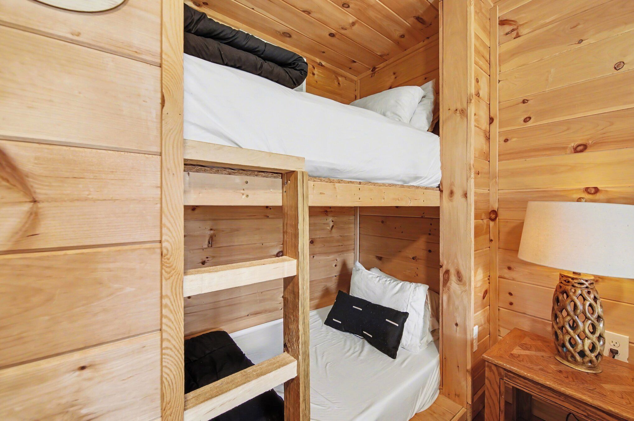 A wooden cabin room with bunk beds, a bedside table, and a lamp.