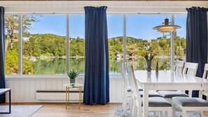 A dining area with a table and chairs, large windows with curtains, a small table with a plant, and a lamp. - 3 bedroom awesome home in Sveio (Sveio)