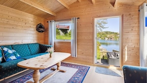 A cozy wooden cabin interior with a sofa, a table, and a view of a lake through a large window. - 3 bedroom awesome home in Sveio (Sveio)