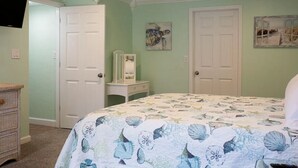 A bedroom with a bed, two doors, a dresser, and artwork on the walls.