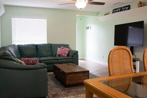 A living room with a green sofa, a wooden coffee table, and a glass dining table.