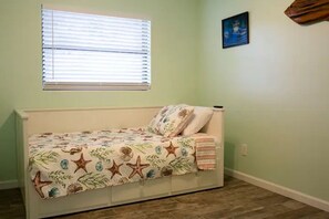 A small bedroom with a bed, a window with blinds, a wall-mounted picture, and a wooden headboard.