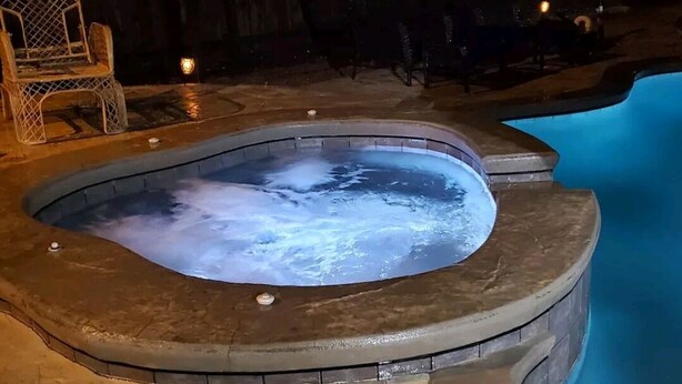 A hot tub with a stone edge, surrounded by a wooden deck and chairs.