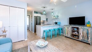 Een moderne keuken met een centraal eiland, barstoelen, een plafondventilator en een televisie op een kast.
