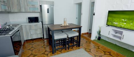 A modern kitchen with a dining area, a flat-screen TV, and a patterned floor.