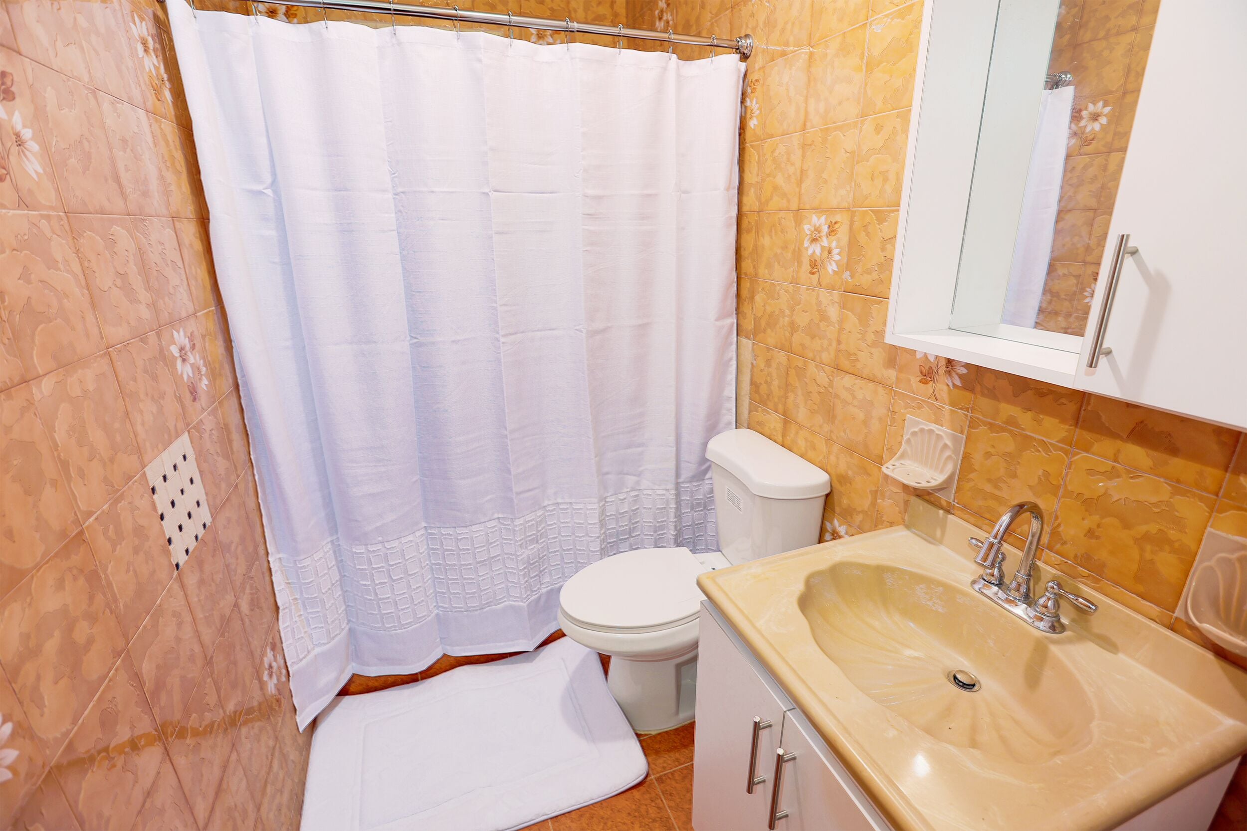 A bathroom with a white shower curtain, a toilet, a sink with a mirror, and tiled walls.
