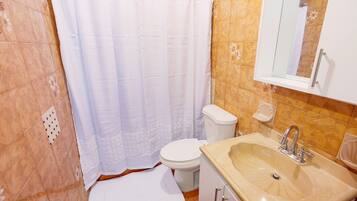 Ein Badezimmer mit weißer Duschvorhang, Toilette, Waschbecken mit Spiegel und Fliesen.