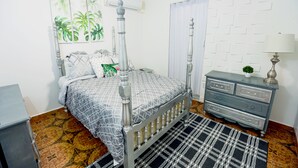 Un dormitorio con cama con dosel, cómoda, alfombra estampada y decoración en la pared.