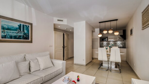Un salon moderne avec un canapé blanc, une table à manger avec des chaises et un coin cuisine équipé d’une cuisinière et de luminaires suspendus.