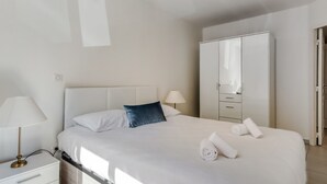 Une chambre d’hôtel bien aménagée, avec un grand lit, une table de chevet, une armoire et une lampe.