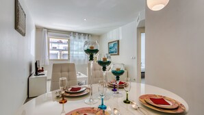 Un coin repas avec une table blanche dressée pour quatre personnes, agrémentée d’assiettes colorées et de serviettes rouges.