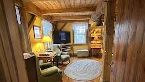 Interior acolhedor de uma cabana com soalho de madeira, televisão, sofá e um abajur.