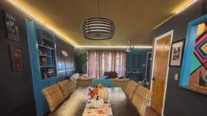 Uma área de refeições com uma mesa de madeira comprida, cadeiras azuis e um corredor decorativo.