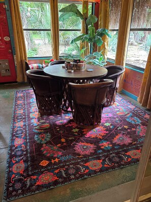 Une table ronde entourée de chaises, un tapis à motifs et une fenêtre avec des rideaux.
