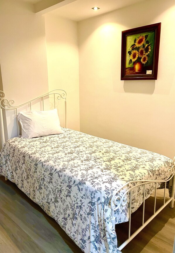 A single bed with a floral bedspread, a white pillow, and a framed painting of sunflowers on the wall.