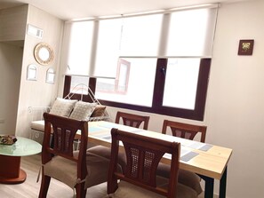 A dining area with a wooden table and chairs, a metal-framed bed, and a window with curtains.