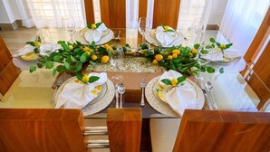 Una tavola da pranzo imbandita per quattro, con tovaglioli bianchi, posate e bicchieri, circondata da sedie di legno.