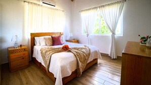 Una camera da letto con un letto in legno, tende bianche, un comò in legno e un comodino con una lampada.