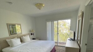 A hotel room with a large bed, a desk, a chair, a window with curtains, and a balcony. - 5 minues to the theme park. Family sized communy pool (Kissimmee)