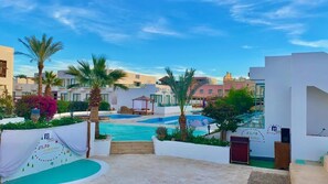 A pool area with a clear sky, palm trees, and a building with a sign. - Badawia Sharm Resort (Sharm El Sheikh)