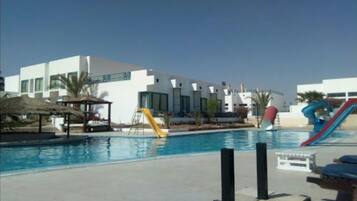 A swimming pool with slides, a thatched-roof structure, and modern buildings in the background.