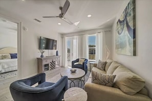 A modern living room with a sofa, chairs, a coffee table, a TV, and a ceiling fan.